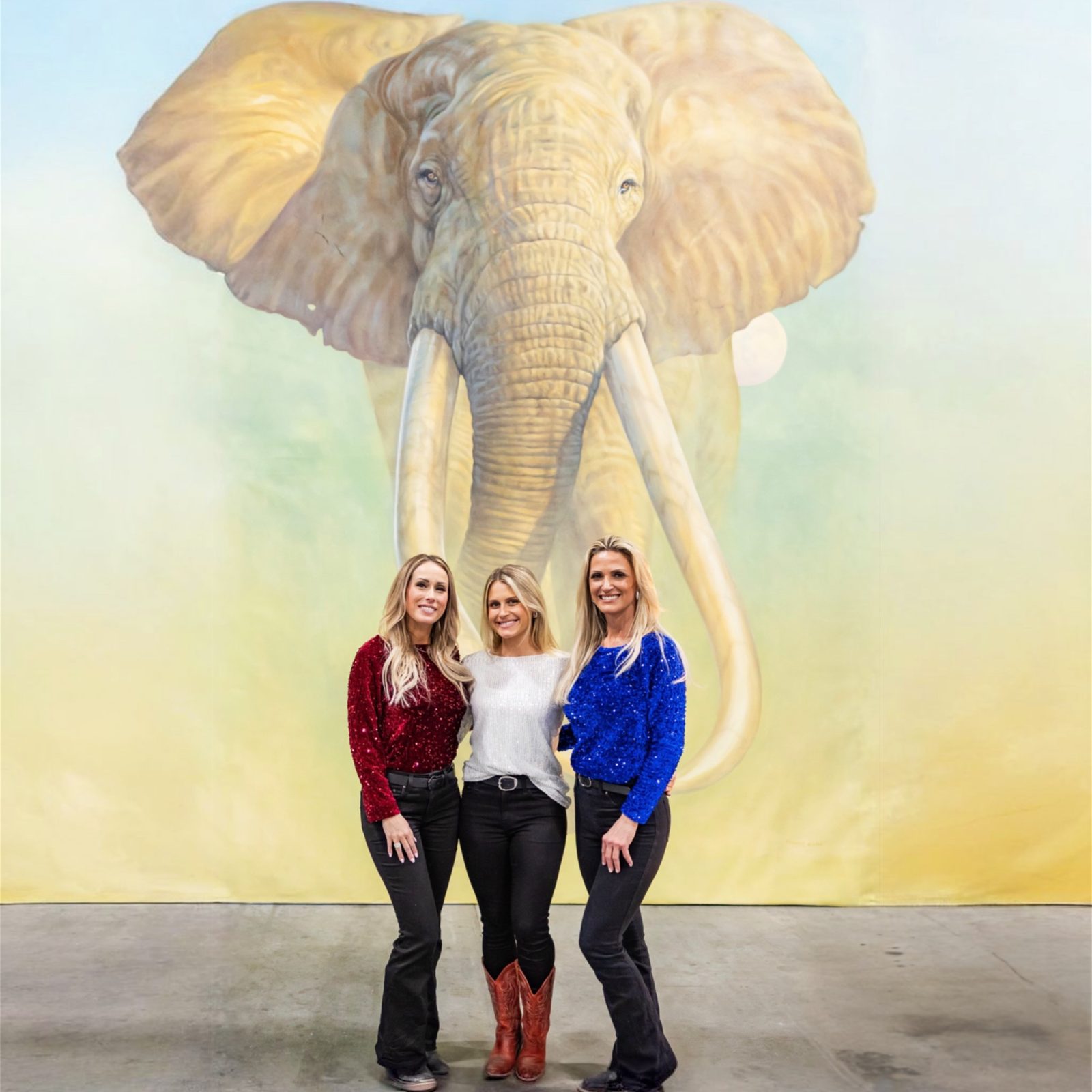 Three Mandi's Models in sequin tops and black jeans in front of a giant painted elephant backdrop