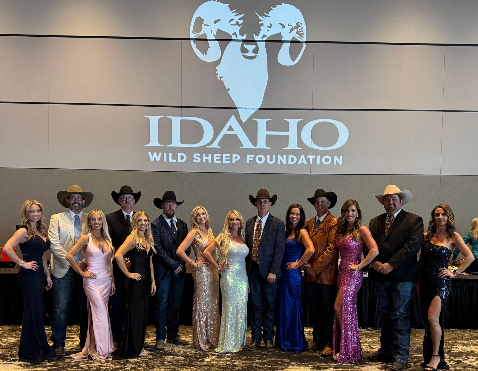 Eight Mandi's Models in gowns with guests in western suits below an Idaho Wild Sheep Foundation logo
